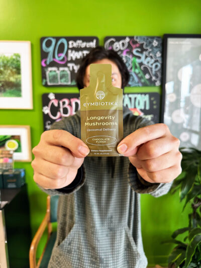 A man holding the green longevity functional mushrooms pouch in front of his face and against a green background with plants.