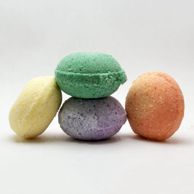 A stack of a miniature, colorful CBD bath bombs. From left to right: Honey Almond, Cucumber Mint, Lavender Vanilla, and Mango Papaya.